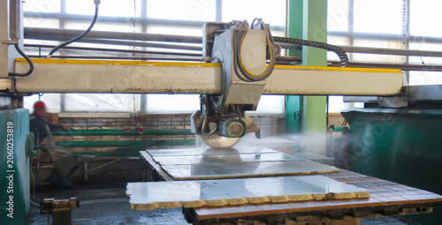 Workers cut stone slabs in a factory with a large cutting machine during daytime