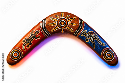 A carved wooden boomerang with intricate Aboriginal art designs is displayed against a white background.