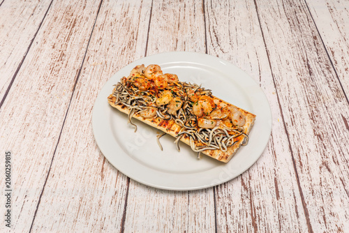 Tableau sur toile Open toast topped with gulas baby eels, shrimp, paprika and parsley sits on a white oval plate over rustic wood
