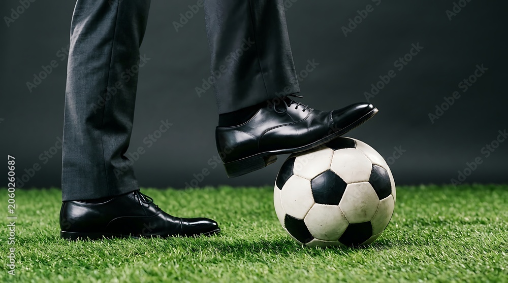 Obraz premium Businessman in formal suit and leather shoes standing with a soccer ball on green grass