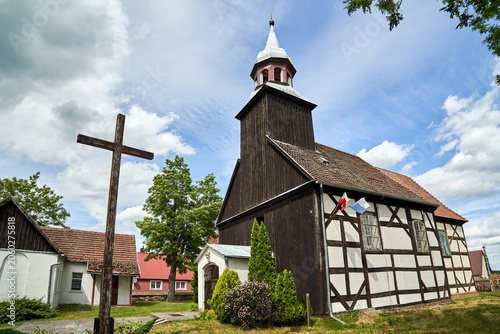 Wooden cross in front of the historic parish church with a bell tower in the village of Kalsko