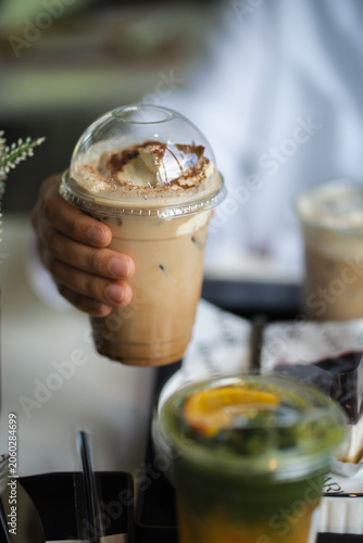 hand of woman holding a take-out iced coffee on black table at cafe.