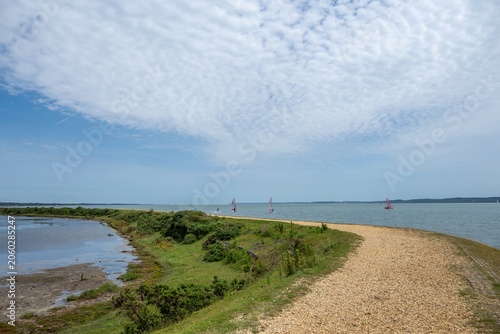 footpath along the Solent Way between Lymington and Keyhaven with the sea blue sky and wispy white clouds in the background