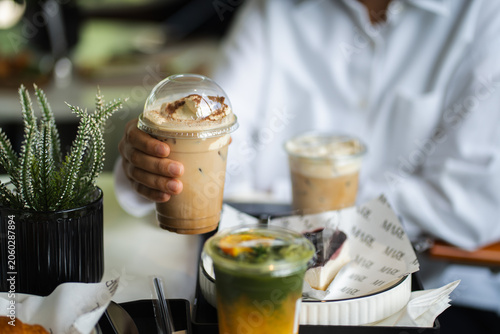 hand of woman holding a take-out iced coffee on black table at cafe.