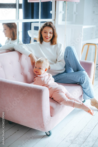 Mother and baby sitting on pink sofa in bright living room