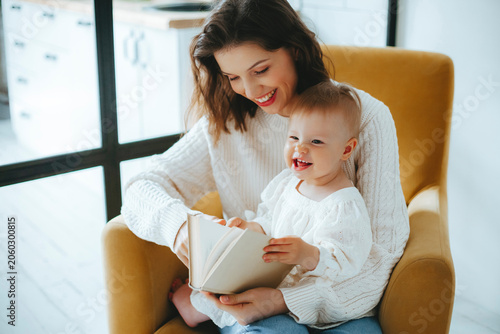 Mother and baby smiling while reading book in modern living room