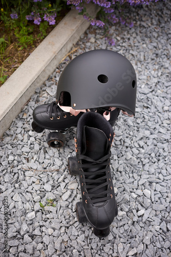 Canvas Print Black roller skates and helmet resting on gravel near blooming flowers in a sunn