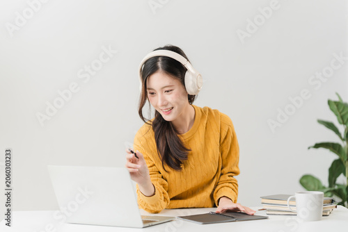 Virtual Learning Experience: A young woman with headphones immersed in online learning, joyfully engaging with her laptop, surrounded by study materials.