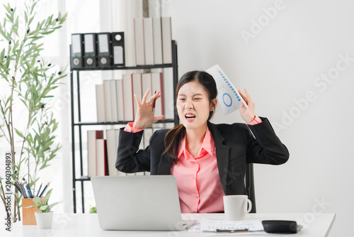 Photos Frustration at Work: A businesswoman looks stressed and overwhelmed as she sits at her desk, clutching papers and showing a look of extreme exasperation