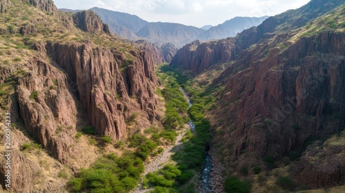 Expansive aerial view of a deep mountain canyon with a winding river and lush green vegetation under a bright sky.
