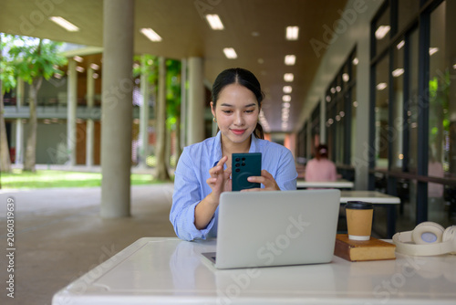 Smiling woman working with smartphone and laptop outdoors