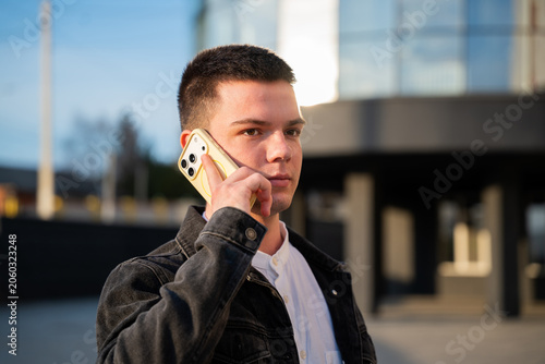 Young businessman talking on a smartphone outside a modern office building in an urban setting. Mobile communication and professional business connectivity for daily work activities