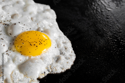 sunny side up egg with sprinkle of black paper and salt cooking on a hot flat top griddle in a commercial kitchen