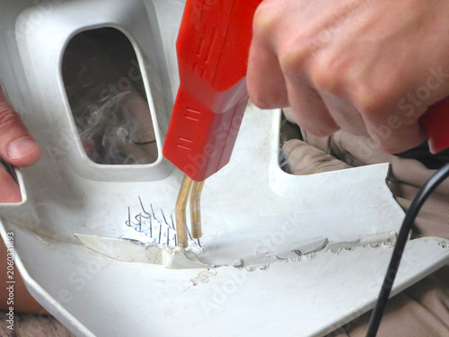 Man repairing plastic bumper with hot stapler tool. Automotive technician fixing crack on car body part. Professional vehicle bodywork and restoration service, maintenance concept.