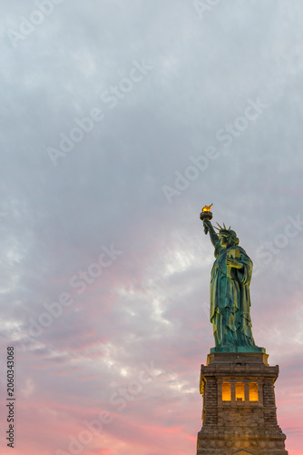 The Statue of Liberty stands against a vibrant sunset sky, serving as an iconic global symbol for travel, tourism, and history at Liberty Island, New York City.