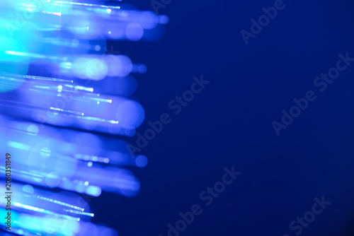 Glowing blue fiber optic tips creating bokeh barrier with large copy space on deep blue background.