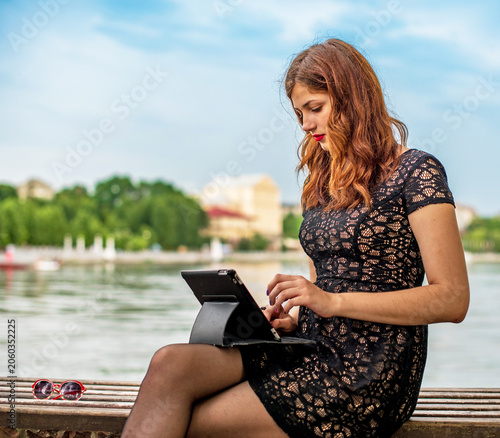 Young pretty girl working on a netbook on a bench in a park near a lake