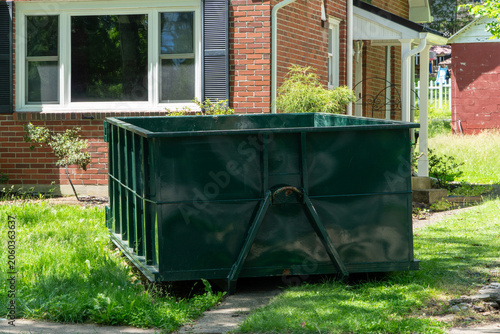 Large Green Roll-Off Dumpster Rental Placed on a Lush Residential Lawn in Front of a Traditional Brick House  Ready for Construction Debris  Home Renovation  or Yard Waste Cleanout Project.