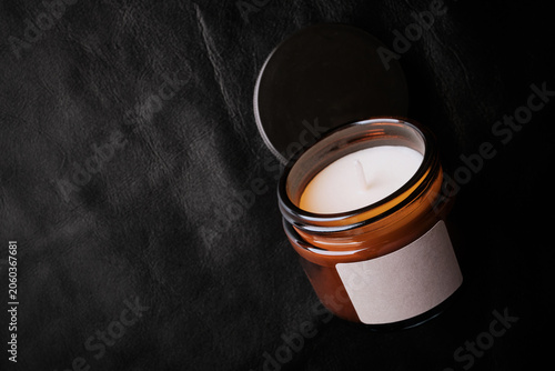 Scented candle in amber jar with white wax and blank label on black leather