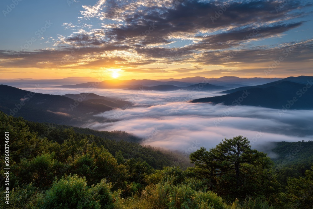 Obraz premium Stunning sunrise over mist-covered mountain ridges with lush green forest in the foreground and dramatic cloudscape illuminating the early morning sky