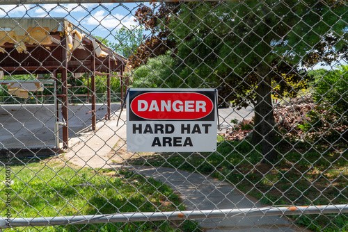 Canvas Print Danger Hard Hat Area sign on a chain link fence, marking a hazardous demolition or construction site with exposed building materials and rubble, emphasizing workplace safety and access