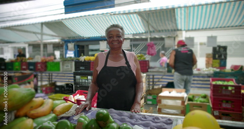 African American elderly woman smiling at outdoor produce market in close portrait expressing warmth life experience and quiet pride within neighborhood street food commerce