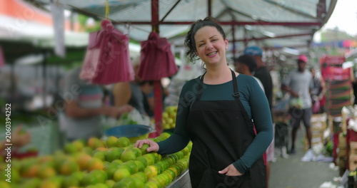 Photography Young woman street vendor smiling at outdoor market stall with fresh produce con