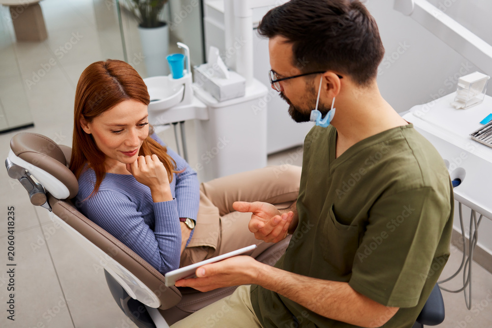 Obraz premium Dentist discussing treatment plan with female patient using tablet