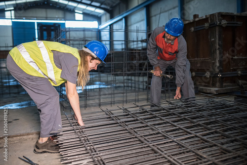 Mature worker helps woman to cut welds of the rebar structure checking its hardness.