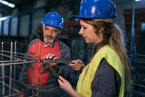 Mature worker helps woman to cut welds of the rebar structure checking its hardness.