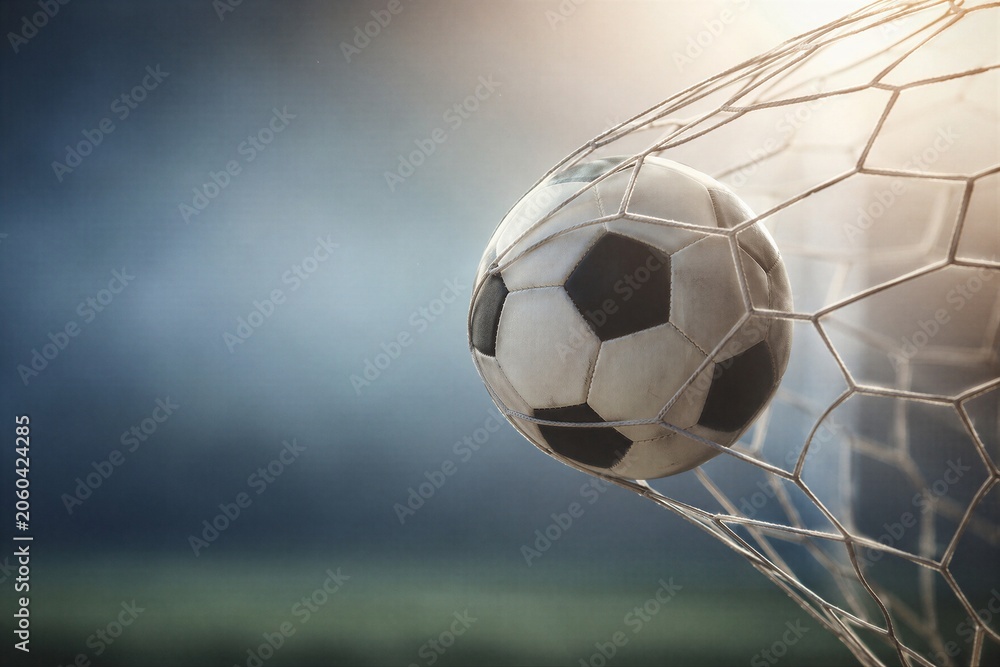 Naklejka premium Soccer ball hitting goal net during match at stadium. Scoring goal in professional championship. Concept of sport victory, competition and active lifestyle. Stadium lighting background