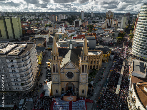 Cathedral Basilica, located in the center of Curitiba, with neo-Gothic architecture. The surroundings feature residential and commercial buildings under a partly cloudy sky.