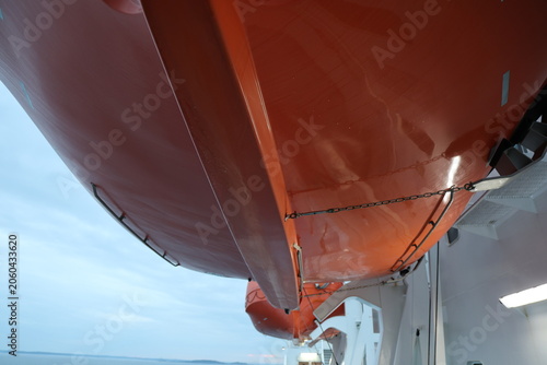 Foto Large orange lifeboat mounted on the side of a ship in Sweden, showing maritime safety equipment and nautical detail
