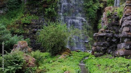 Tranquil Waterfall With Lush Surroundings, Serene Waterfall Flowing Beneath Stone Bridge Amidst Vibrant Woods