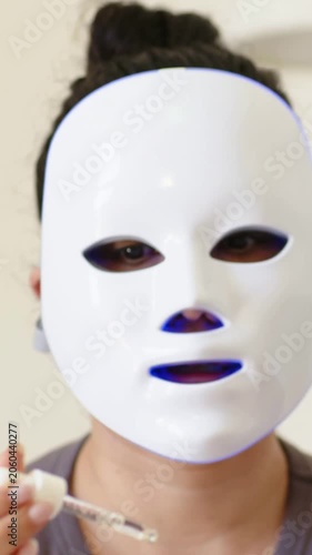 Vertical video: Uncapping serum, LED-mask tech dispensing drops onto client forehead for skincare