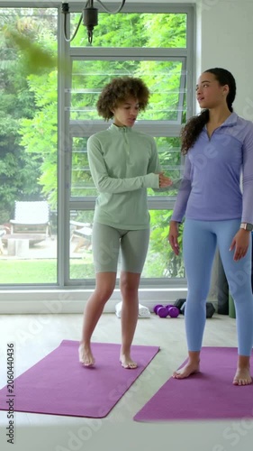 Vertical video: Cueing coach in mint top guiding student into fold to align at home on purple mats