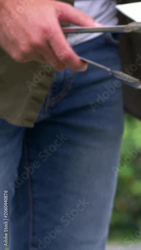 Vertical video: Hand entering cook in striped T flipping patties on yard grill for meal with tongs