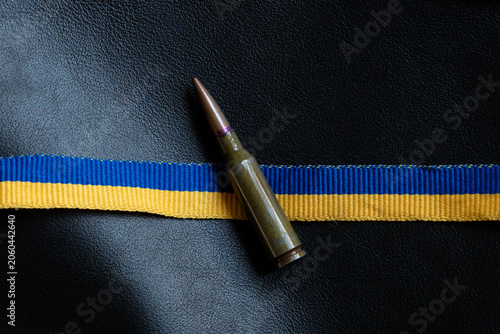 A cartridge against a ribbon in the colors of the Ukrainian flag, on black leather, on the theme of defense, the army, military service