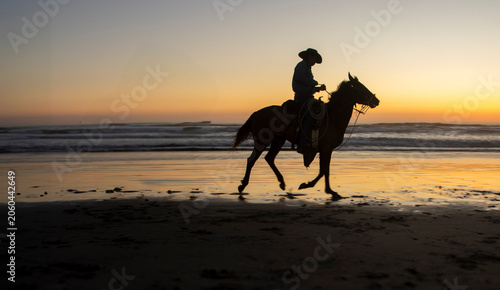 Silhouette of a cowboy on horseback at a beach at sunset