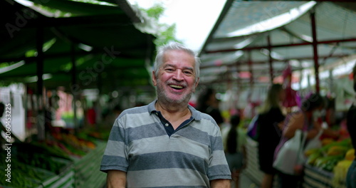 Obraz na plátne Elderly man smiling broadly at camera at outdoor market conveying joy friendline