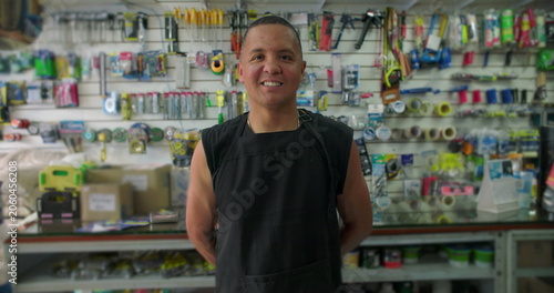 Фотография Hispanic hardware store worker smiles gently in shop aisle expressing pride appr