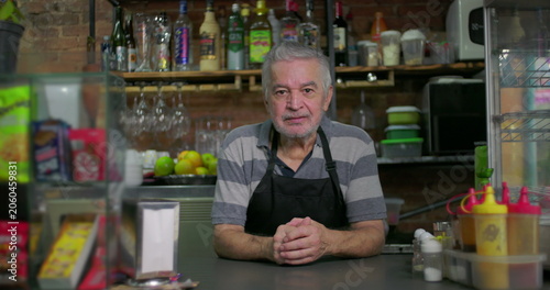 Photography Older café owner leaning forward behind counter with hands clasped conveying att