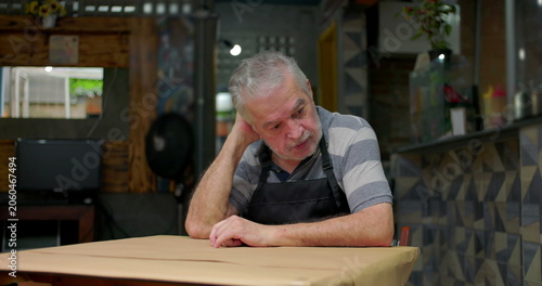 Concerned small business owner sits alone at table showing despair uncertainty and emotional weight of struggling to sustain neighborhood café during hard economic times