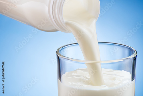 Canvastavla Close-up of milk pouring in drinking glass from plastic bottle on blue backgroun