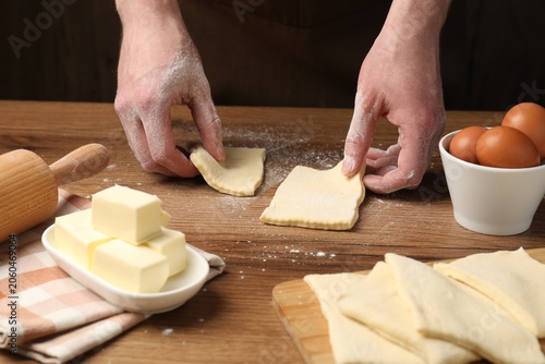 фотографія Man with raw puff pastry dough at wooden table, closeup