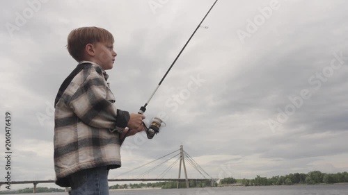 A little boy is fishing on a big river using a spinning rod
