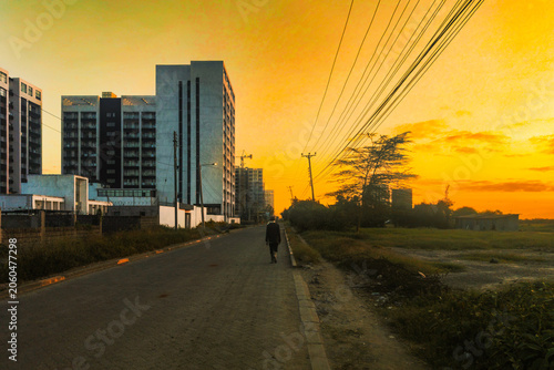 Scenic view of a Man Walking on Suburban Street amidst Modern Residential Towers against a Golden Sunset in Syokimau, Kenya