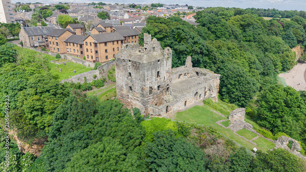 Obraz premium Scenic view of the ruined historic Ravenscraig Castle fortress surrounded by green trees and traditional houses in Fife, Scotland.