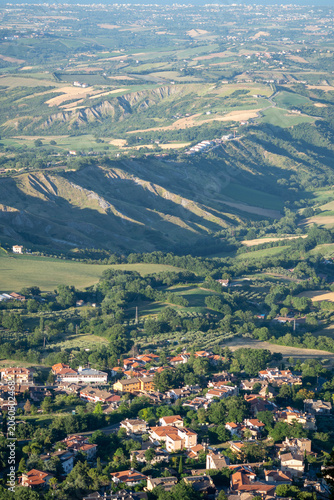Aerial view of a small village nestled among green hills, fields and wooded countryside in warm evening light.