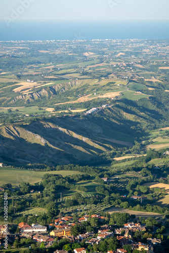 Aerial view of a small village nestled among green hills, fields and wooded countryside in warm evening light.